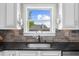 A kitchen sink with a black countertop and backsplash with a view outside the window at 5950 Hidden Ridge Ct, Cumming, GA 30028