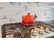 Close up of a modern stove with a red tea kettle on top and a decorative tile backsplash at 4360 Havenridge Pl, Cumming, GA 30041