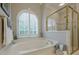 Bright bathroom featuring a soaking tub beneath a large arched window, with a glass shower at 1364 Gulfport Run, Grayson, GA 30017