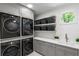 Modern laundry room with gray cabinets, stacked washer and dryer, and open shelving with gray wicker baskets at 5260 Long Island Nw Dr, Atlanta, GA 30327