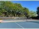 Bright, blue tennis court with green trees and black fencing under a clear sky. A nice amenity for this community at 630 Bluff Oak Ct, Roswell, GA 30076
