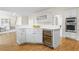 A kitchen island with white cabinets, drawers, stainless steel wine cooler, and white countertop on hardwood flooring at 1100 Kensington Ct, Johns Creek, GA 30022