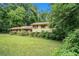 View of single Gathering home surrounded by mature trees and an overgrown front yard at 2214 River Rd, Ellenwood, GA 30294