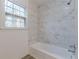 Bathroom with a white tub, marble tile surround, and a bright window at 4639 Hardwood Rd, Stone Mountain, GA 30083