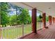 Expansive covered porch with brick pillars, wooden deck, and white railing showcasing the lush greenery at 7180 Westray Rd, Cumming, GA 30028