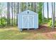 Light blue storage shed with white trim and double doors nestled amongst tall trees in a lush yard at 505 Alta Ct, Villa Rica, GA 30180
