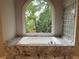 Soaking tub with marble tile surround under an arched window with a view of mature trees at 870 Thornberry Dr, Alpharetta, GA 30022