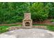 Stone outdoor fireplace with seating, surrounded by a lush green yard and mature trees at 4825 Brighton Lake Dr, Cumming, GA 30040