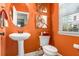 Charming half bathroom with bright orange walls, pedestal sink, round mirror, and natural light from the window at 3567 Sycamore Bnd, Decatur, GA 30034