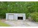 Metal storage building with two garage doors and a concrete pad in front surrounded by a lush green forest at 3785 Willow Ridge Rd, Douglasville, GA 30135