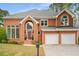 Classic brick home with an arched entryway, lush landscaping, and a spacious two-car garage at 710 Glen Royal Dr, Roswell, GA 30076