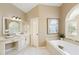 Bright bathroom featuring a soaking tub, arched window, and vanity with a marble countertop and decorative mirror at 710 Eastbourne Ct, Alpharetta, GA 30005
