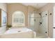 Bright bathroom featuring a soaking tub, glass-enclosed shower, neutral tile and an arched window for natural light at 710 Eastbourne Ct, Alpharetta, GA 30005