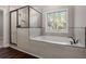 A tiled bathtub with a dark faucet and glass enclosed shower near a window at 1874 Mcgarity Rd, Mcdonough, GA 30252