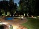Outdoor pool and spa with brick surround, lush landscaping, and ambient lighting for evening enjoyment at 5475 Copper Creek Pass, Cumming, GA 30040