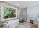 Serene bathroom with soaking tub, glass shower, and marble-look accent wall and green view at 7750 Landowne Dr, Atlanta, GA 30350