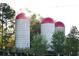Three large farm silos with red dome tops standing tall, surrounded by lush greenery in a serene countryside setting at 1210 Mayfield Rd, Milton, GA 30009