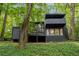 Modern home boasts dark exterior, balcony, and walls of windows amongst mature trees at 5020 Vallo Vista Ct, Atlanta, GA 30342