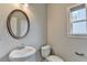 Compact bathroom with pedestal sink, oval mirror, and toilet beneath a bright window at 6468 Pierless Ave, Sugar Hill, GA 30518