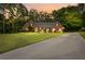 Inviting brick home with a well-manicured lawn and long driveway, surrounded by mature trees, at sunset at 2297 Ironwood Hill Ct, Dacula, GA 30019