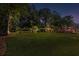Evening view of a large backyard with manicured lawn, enhanced by landscape lighting and flowering shrubs at 1440 Water View Ln, Suwanee, GA 30024