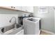Bright laundry room features a stainless steel sink, white cabinetry, countertop, and a modern washer and dryer unit at 1440 Water View Ln, Suwanee, GA 30024