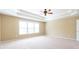 Carpeted bedroom showcases tiered ceiling trim, a modern ceiling fan, and large windows for bright, natural light at 335 Roberts Run Cv, Suwanee, GA 30024