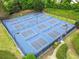 Aerial view of eight well-maintained blue tennis courts with lights and surrounded by green trees at 912 Santa Anita Dr, Woodstock, GA 30189