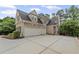Rear view of brick home featuring an attached two-car garage and a manicured backyard at 5293 Aldeburgh Dr, Suwanee, GA 30024