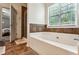 Inviting bathroom featuring a soaking tub next to a window, tile accents, and a door leading to the bedroom at 301 Downing Creek Trl, Canton, GA 30114