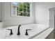 Close-up of a modern bathtub with black fixtures and tiled surround under a window at 1909 Riverlanding Cir, Lawrenceville, GA 30046