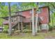 View of the rear of the red home with wooden deck, surrounded by nature and lush greenery in the background at 5419 Tyree Rd, Winston, GA 30187