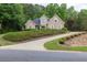 Beautiful tan home featuring a curved driveway, lush landscaping, and mature trees in the background at 1720 Ivey Trce, Cumming, GA 30041