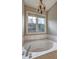 The soaking tub is surrounded by marble and features a light-up chandelier in a luxurious bathroom at 604 Lexington Way, Woodstock, GA 30189