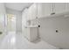 Bright laundry room with white tile floors, cabinets, sink, and access to other rooms at 2645 Preston Ridge Ln, Dacula, GA 30019