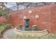 Decorative fountain with lion head spouts set against a brick wall with garden plants, creating a peaceful ambiance at 12084 Cotton Aly, Alpharetta, GA 30009