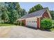 View of a two-car garage with red brick and a driveway surrounded by green trees and a blue sky at 2903 Southpark Sw Ter, Conyers, GA 30094
