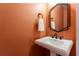 A modern half-bathroom featuring a pedestal sink, geometric mirror, and orange walls at 988 Gentry Sw Ln, Marietta, GA 30064