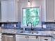 Bright kitchen features a stainless steel sink, blue tiled backsplash, and white cabinetry with natural light at 5105 Tynewick Ne Trce, Roswell, GA 30075