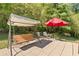 Seating area on stone patio features a red umbrella, bench swing with canopy, and lush green trees at 5360 Franklin Goldmine Rd, Cumming, GA 30028