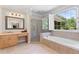 Bright bathroom featuring a soaking tub under a window, glass shower, and wood vanity at 5360 Franklin Goldmine Rd, Cumming, GA 30028