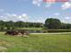 Picturesque view of a rural landscape with a pond, mature trees, and antique tractor on a sunny day at 4143 N Swann St, Covington, GA 30014
