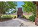 An outdoor brick fireplace on a concrete patio is framed by shade trees and green space at 1257 Park Pass Way, Suwanee, GA 30024