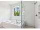 Bright bathroom featuring a tiled bathtub, glass-enclosed shower, and large window at 6925 Colfax Ave, Cumming, GA 30040