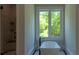 Elegant bathroom with a freestanding tub and a window with views of lush, green trees at 10765 Shallowford Rd, Roswell, GA 30075