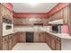 Vintage kitchen with wood cabinets, black appliances, tiled countertops, and floral wallpaper at 4953 Mcpherson Ne Dr, Roswell, GA 30075