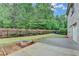 Grassy backyard featuring wooded perimeter with black fence, in-ground fire pit, and concrete patio at 9270 Colham Dr, Cumming, GA 30041