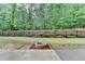 Grassy backyard featuring wooded perimeter with black fence, in-ground fire pit, and concrete patio at 9270 Colham Dr, Cumming, GA 30041