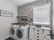 A modern laundry room features stylish wallpaper, a front-load washer and dryer, and a white cabinet at 4790 Epps Ln, Cumming, GA 30040