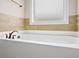 Soaking tub surrounded by neutral ceramic tiles and a small window offers a serene and relaxing bathing experience at 100 Nemoura Ct, Fairburn, GA 30213